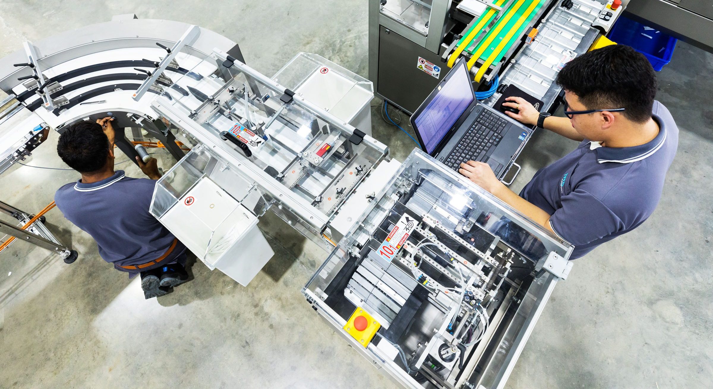 Technical specialists work on an automated production system and check machine parameters via a laptop interface.