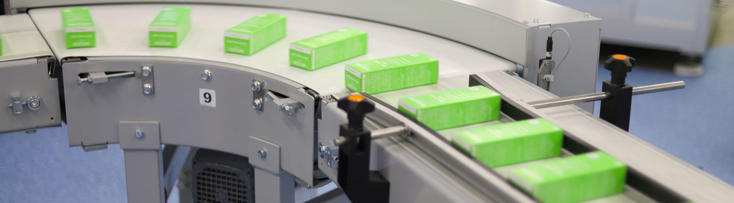 Grüne Faltschachteln auf einem gebogenen Förderband in einer Produktionslinie.