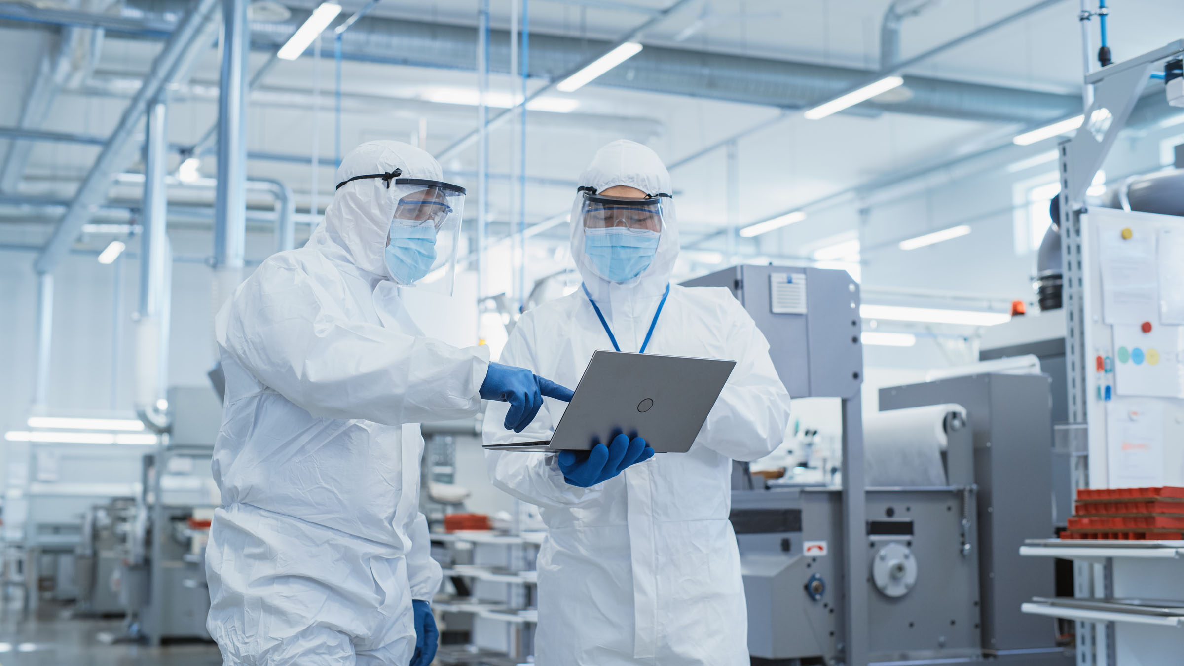 Cleanroom environment with two technical specialists checking production data on a mobile laptop.