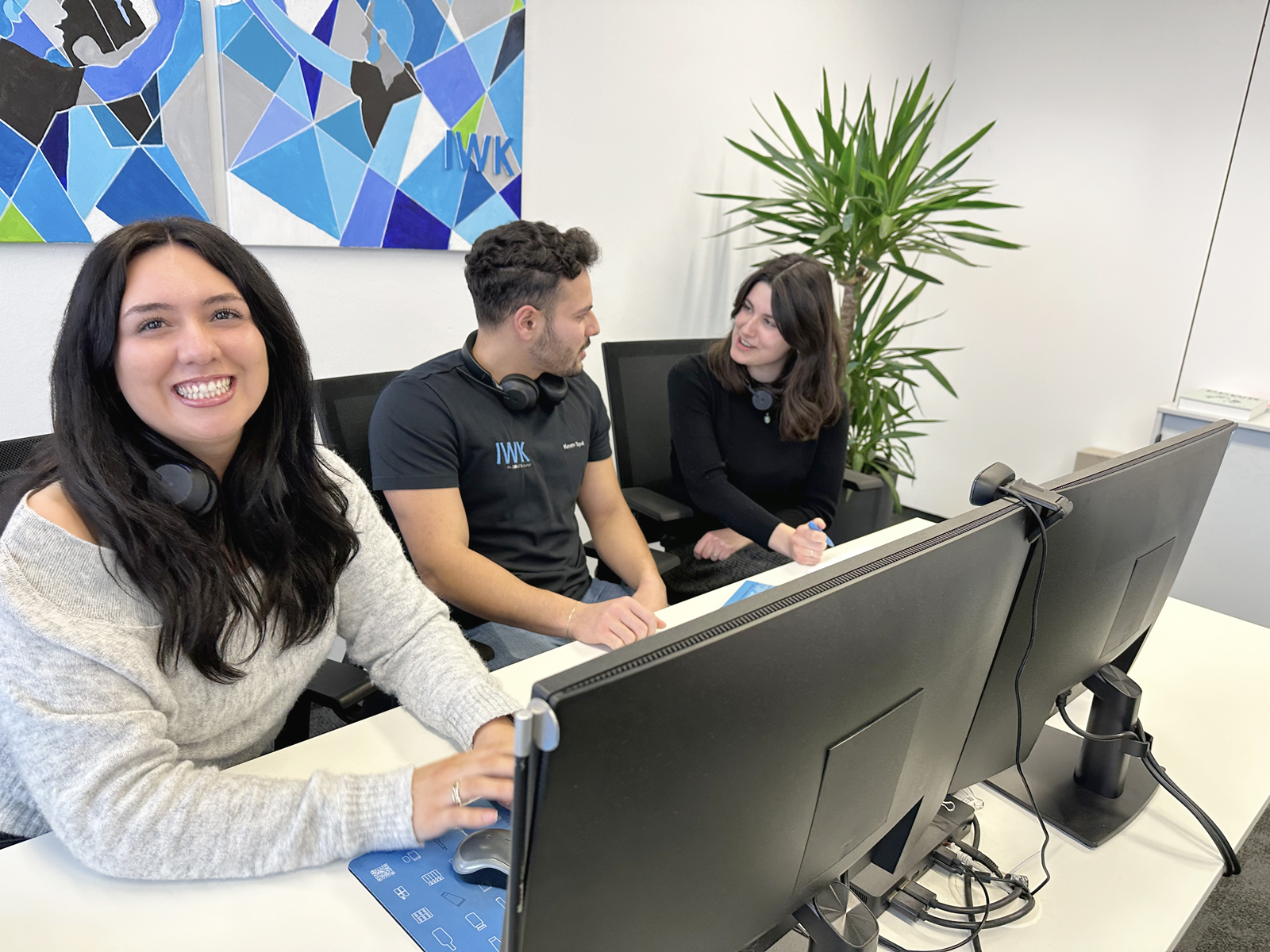 Mitarbeitende in einem modernen Büro im fachlichen Austausch vor zwei Monitoren.