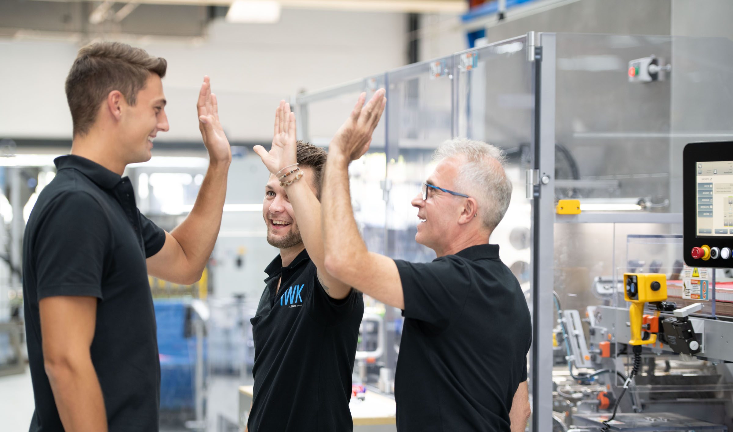 Drei Personen im Produktionsumfeld, die gemeinsam einen erfolgreichen Moment feiern.