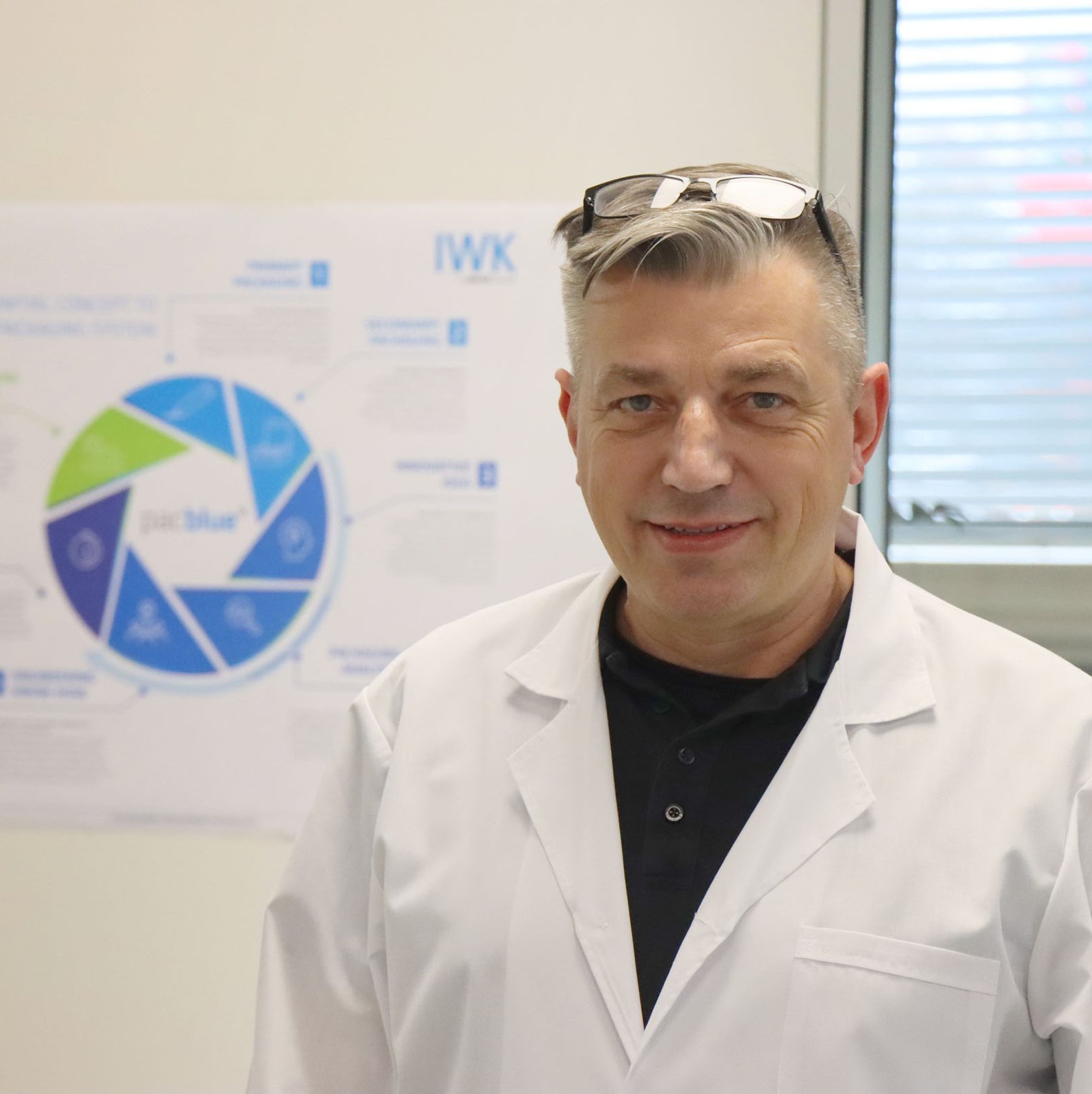 Person im Laborkittel steht vor einem Poster mit Nachhaltigkeits- und Prozessgrafiken in einem Laborraum.