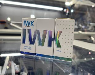 Three IWK folding boxes with holographic design on a reflective glass surface.