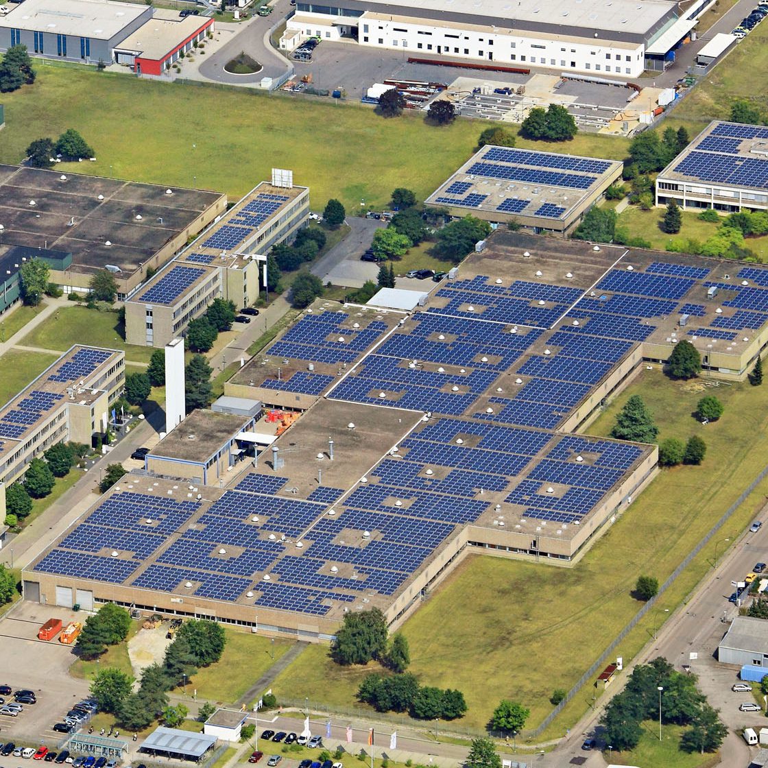 Luftaufnahme eines modernen Industrieareals mit großflächigen Photovoltaikanlagen auf den Hallendächern.
