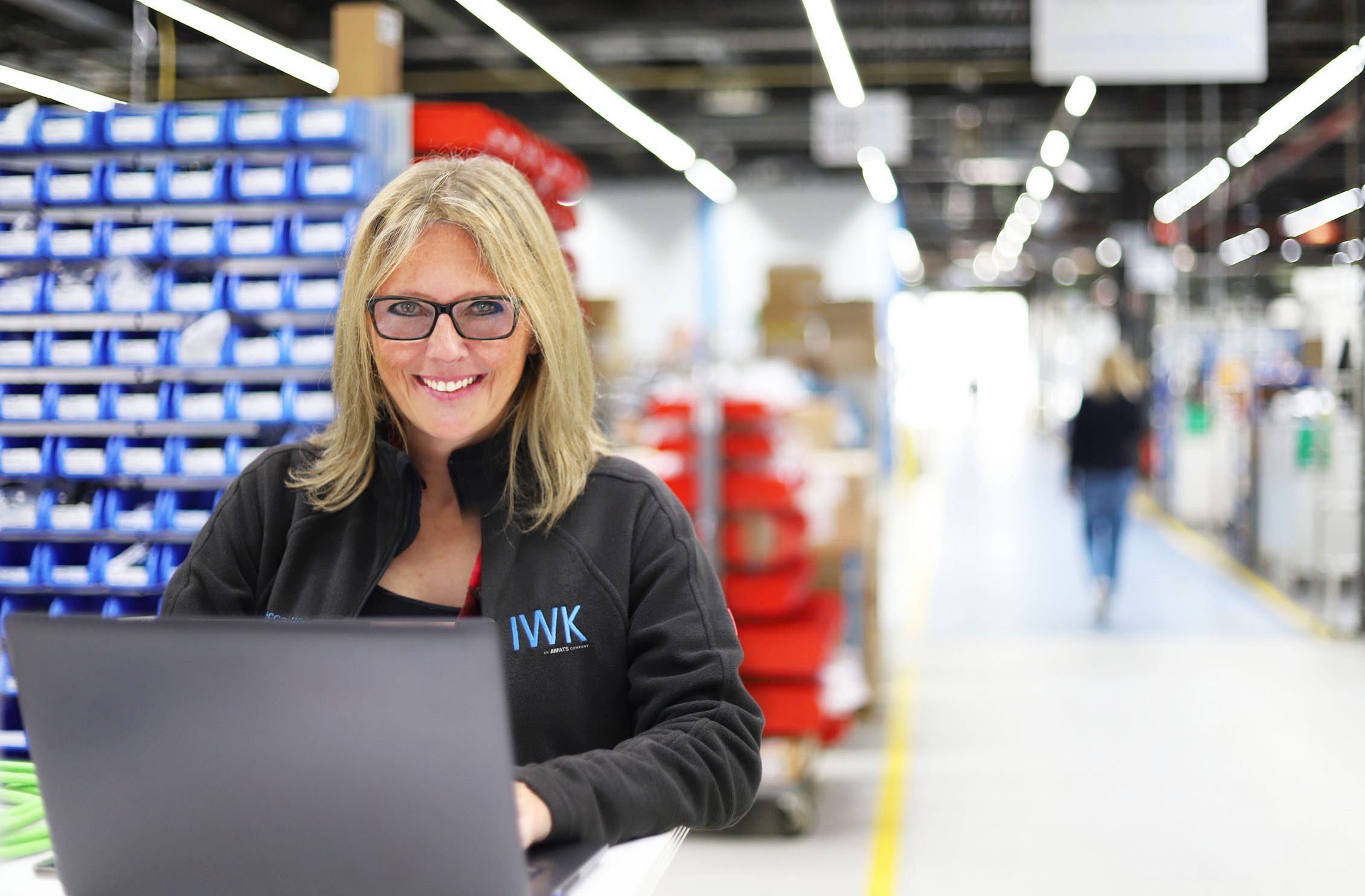 Person working with laptop in a production environment with IWK clothing.