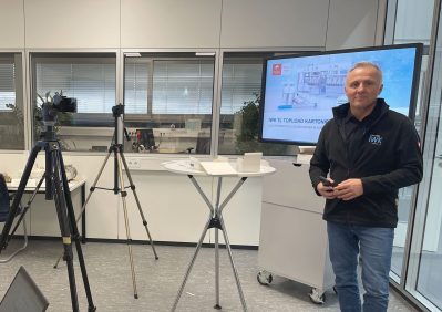Person presenting technical content in front of a large display in a modern meeting room.