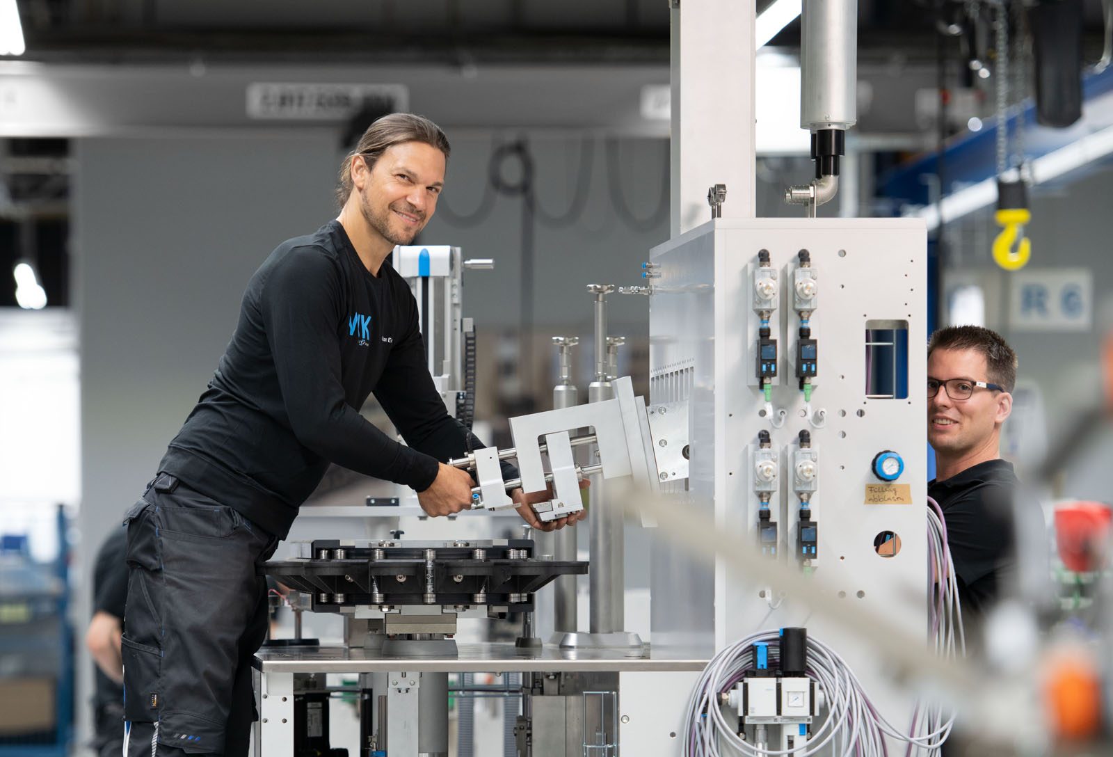 Technische Fachkraft steht an IWK Tubenfüllmaschine mit Dosierstation und Transportsegmenten.