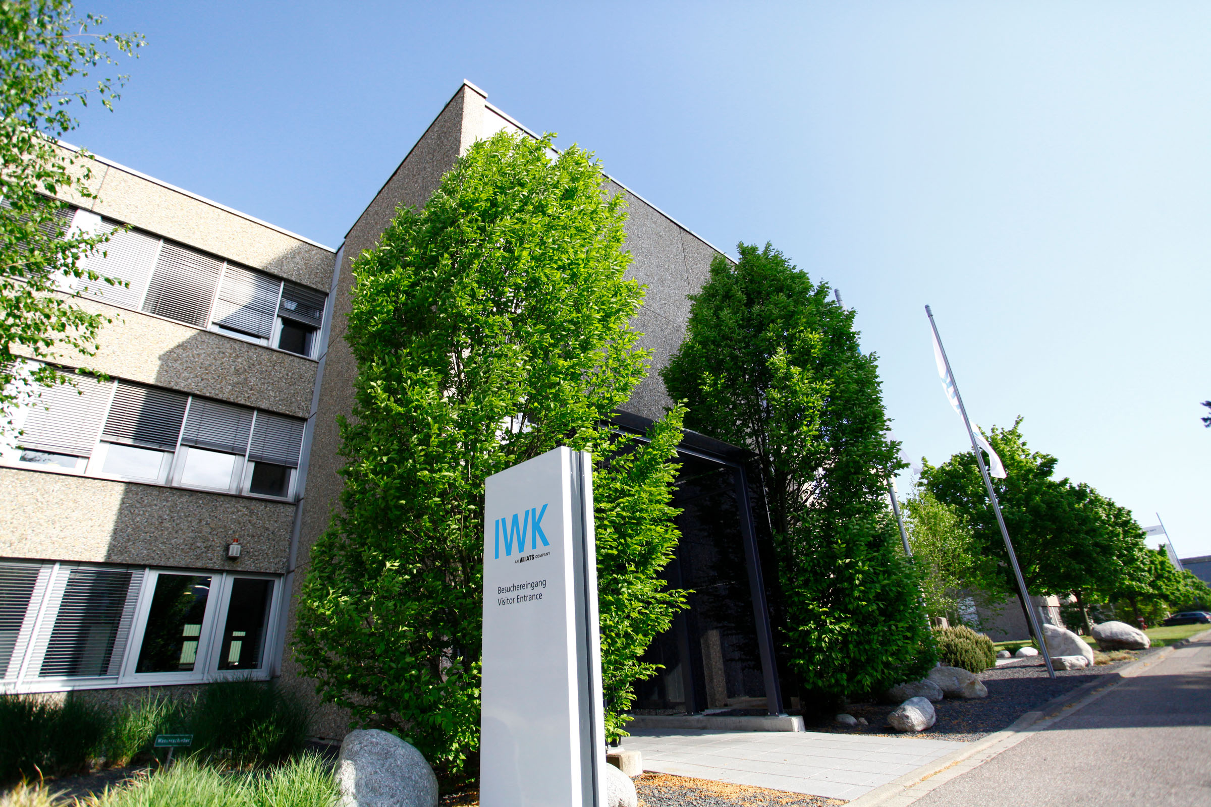 Entrance area of the IWK company building with company stele and surrounding greenery.