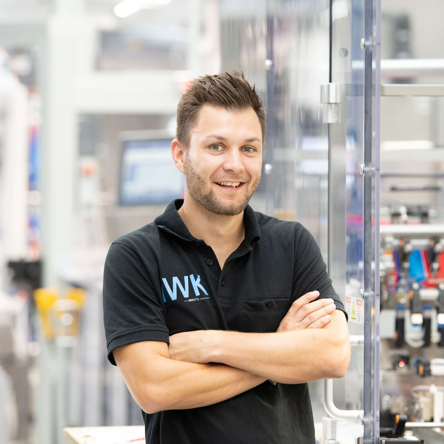 Person in IWK‑Arbeitskleidung steht vor einer Maschinenlinie in der Produktion.