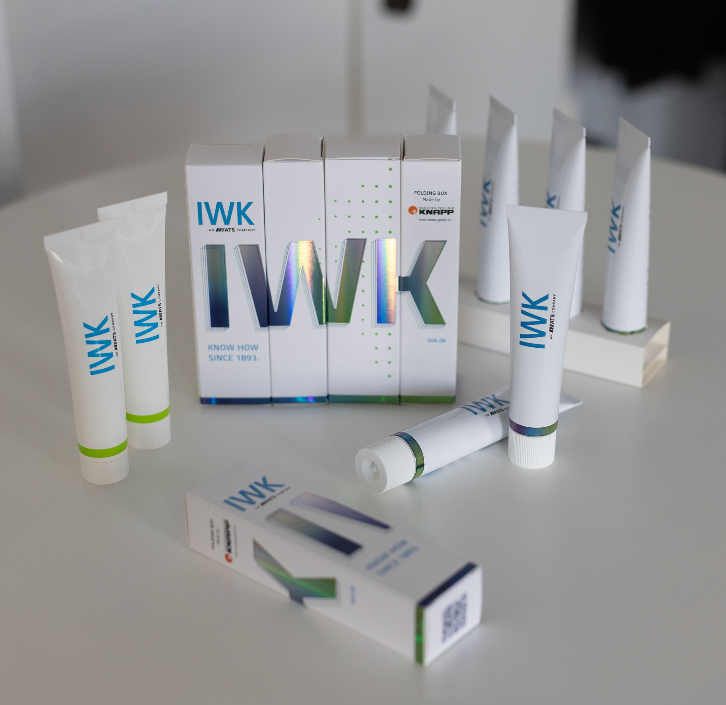 IWK tube and folding carton packaging arranged on a white table.