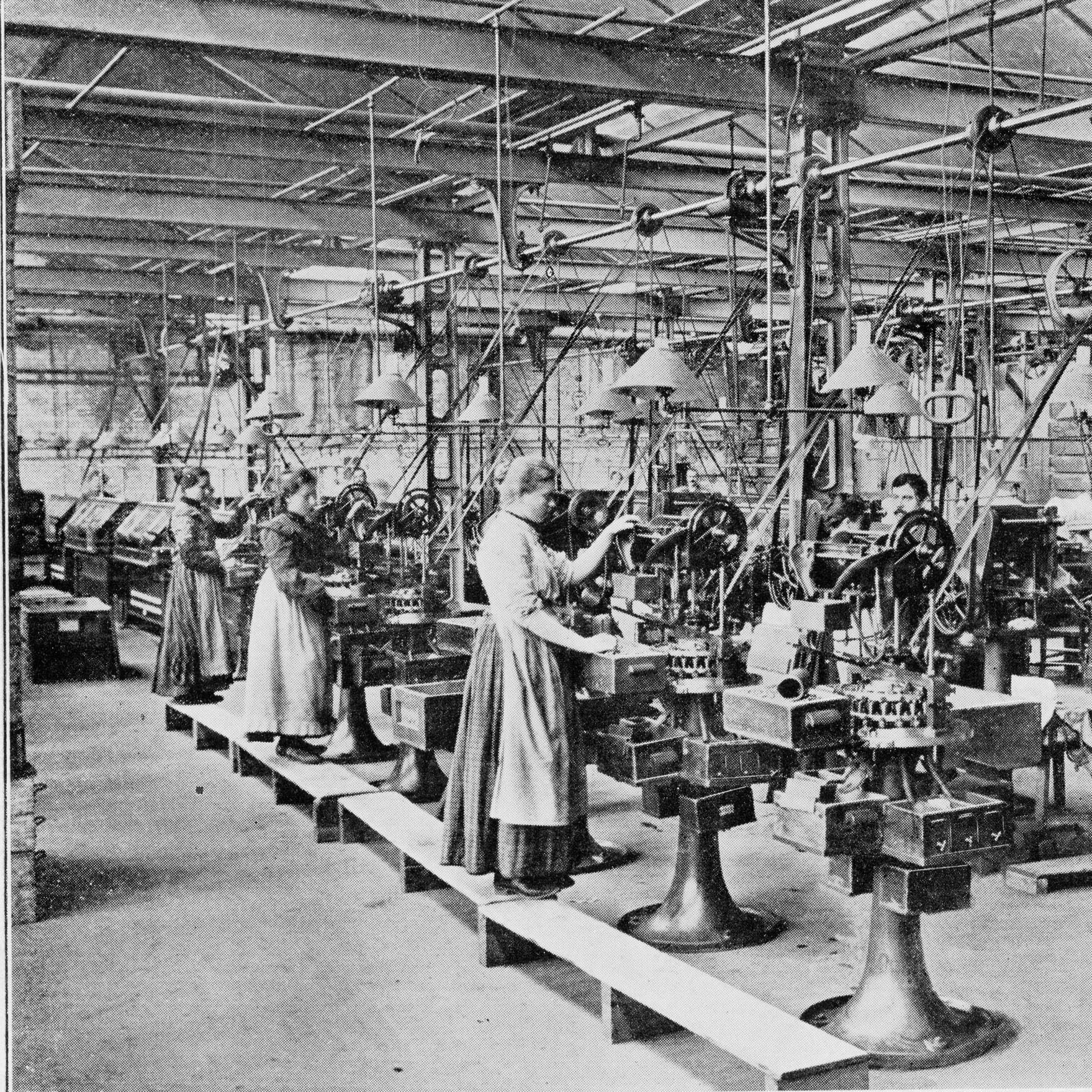 Historische Produktionshalle mit mechanischen Fertigungsmaschinen und mehreren Arbeitenden während eines frühen Industrialisierungsprozesses.
