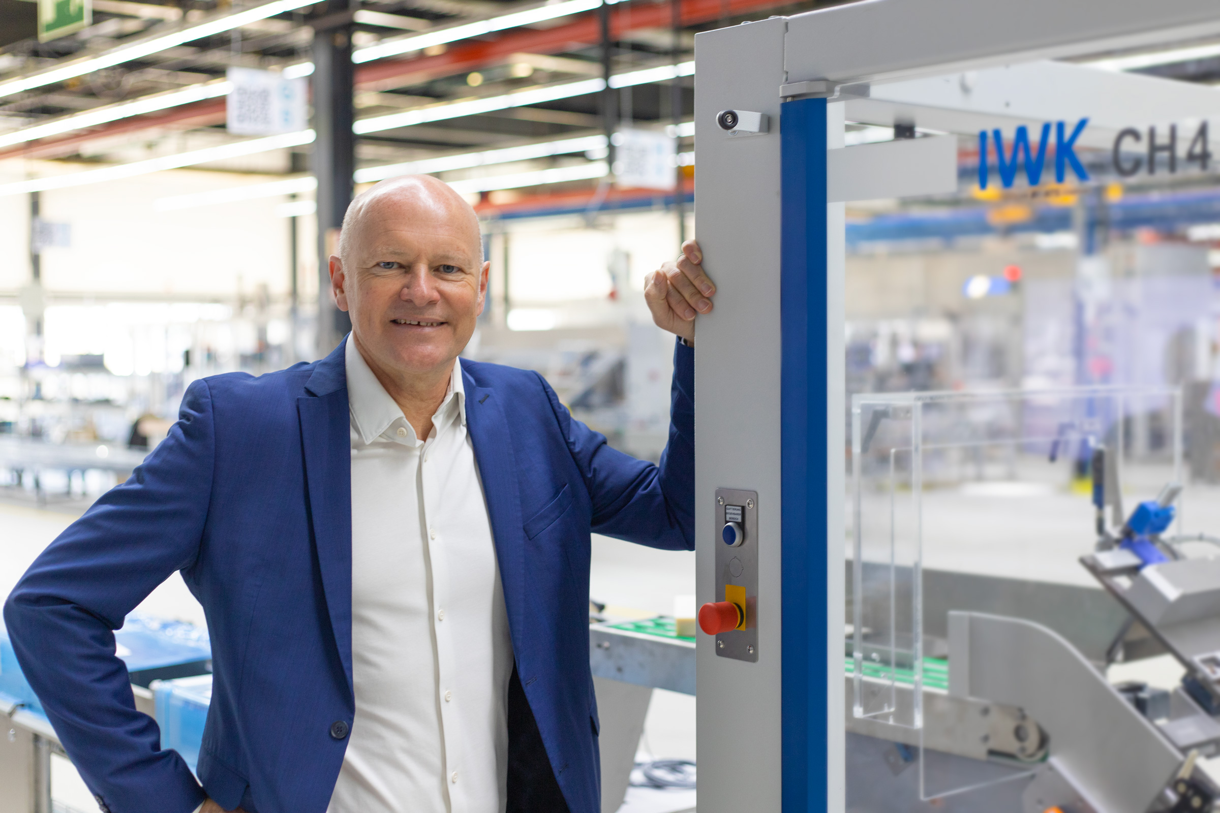 President der IWK Gruppe im blauen Anzug steht am IWK-Kartonierer CH4 in der modernen IWK Produktionshalle