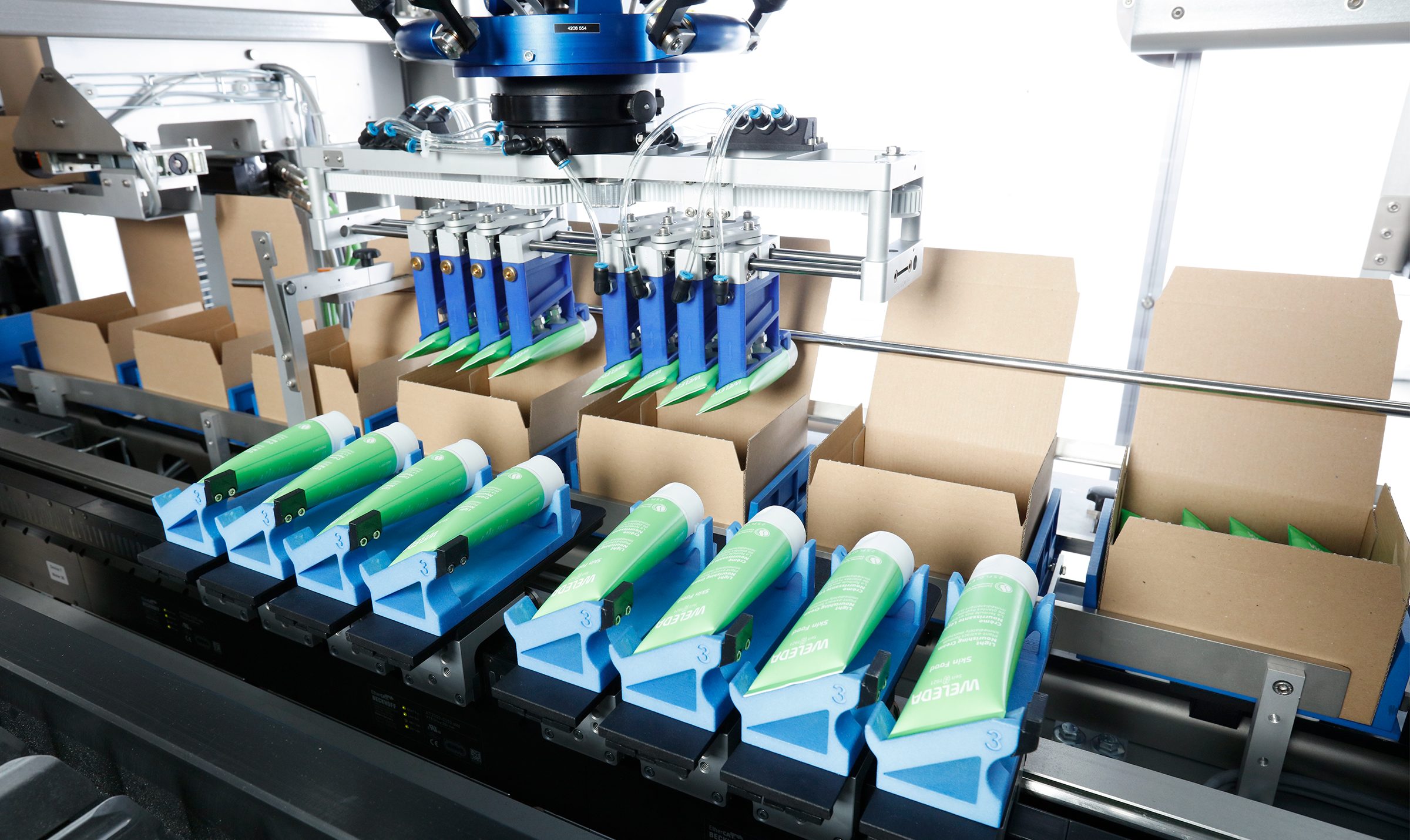 Automatisiertes Verpackungssystem mit Greifmodul, das Tuben präzise in offene Kartons einsetzt.